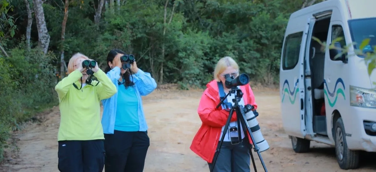 Birdwatchers using binoculars and a spotting scope beside the tour van
