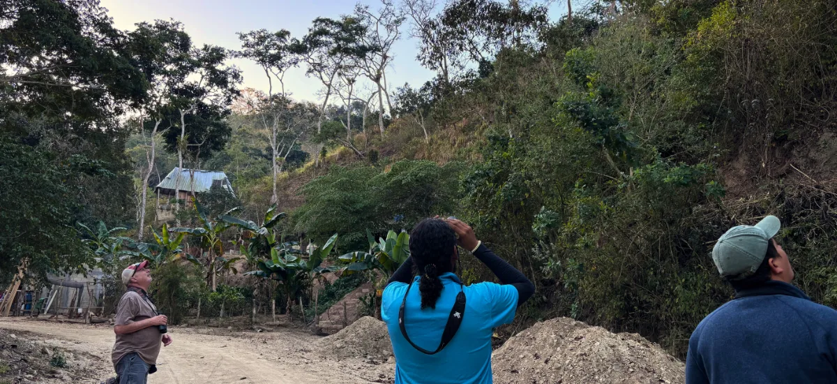 Guide and travelers birdwatching along a dirt road near a hillside village
