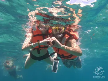 Couple snorkeling and making a heart shape with their hands underwater at Los Arcos