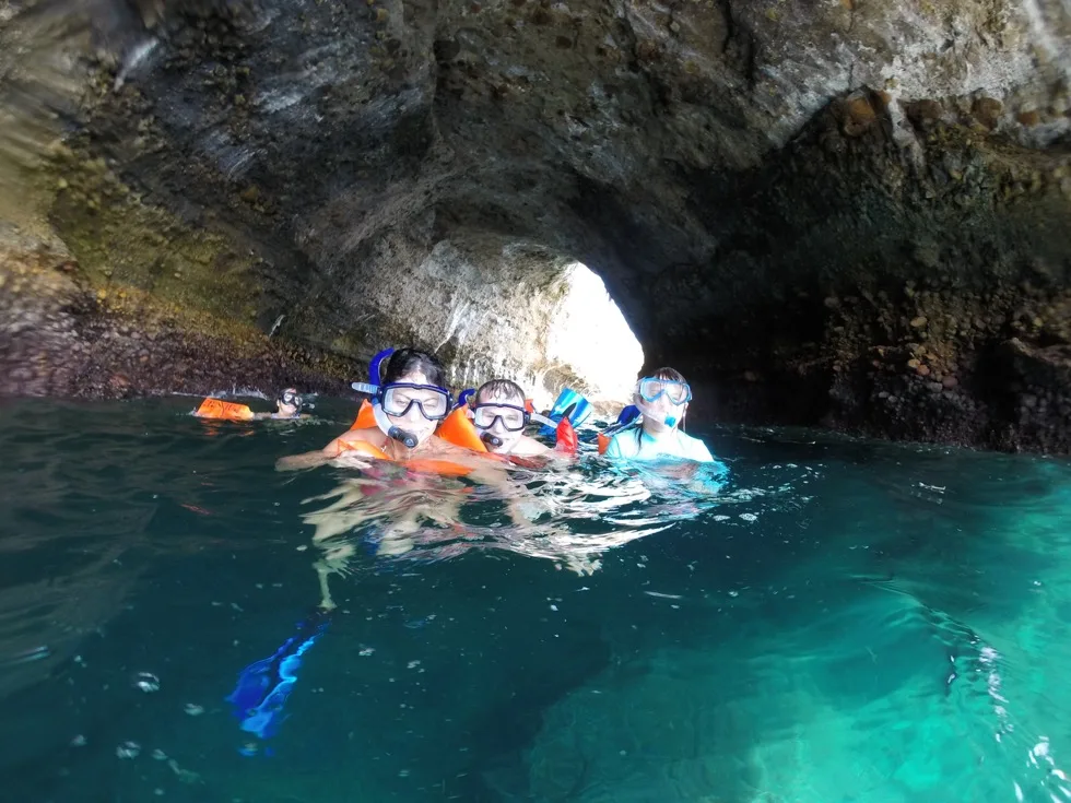 Snorkelers swimming through a rock tunnel at Los Arcos