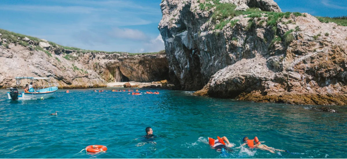 Snorkelers swimming in the turquoise cove next to the sea cave at Islas Marietas