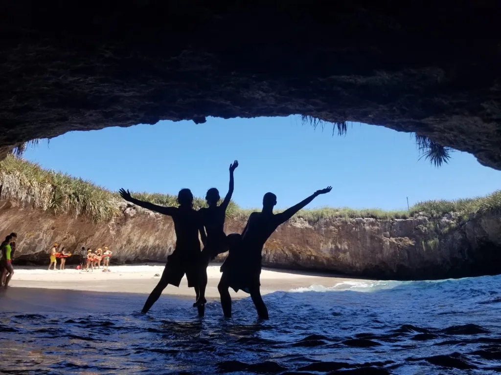 Friends celebrating on the hidden beach, silhouetted against the sea cave