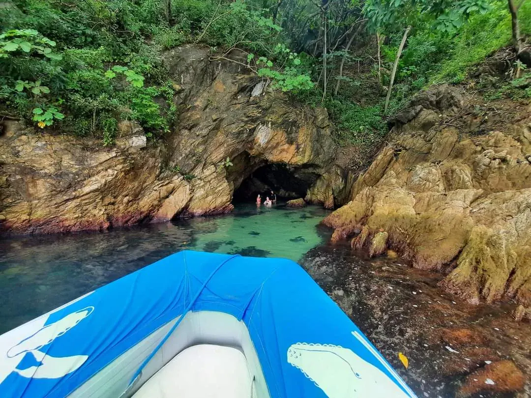 Boat approaching a sea cave along the coast, with swimmers exploring inside