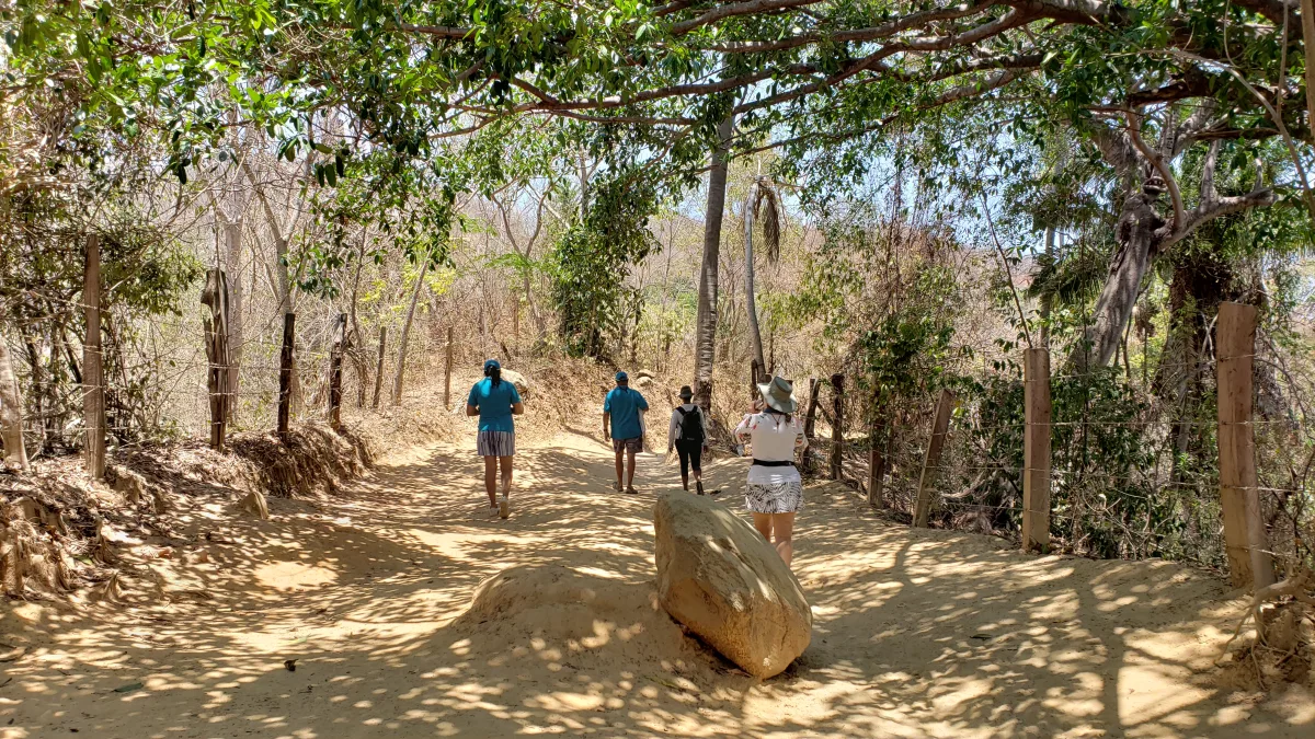 Hikers walking a sandy trail past a large boulder