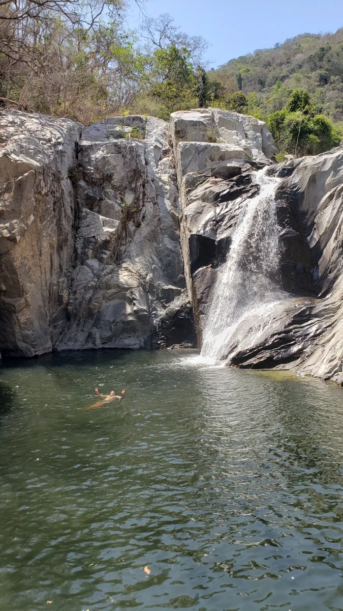 Guest swimming below the falls, giving a peace sign