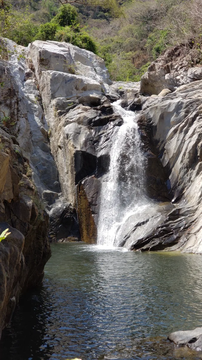 Tall waterfall cascading over layered rock into a clear pool