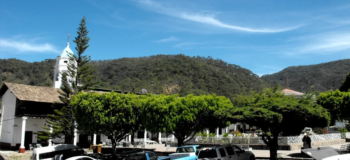 Main square and church of San Sebastian del Oeste with forested mountains behind