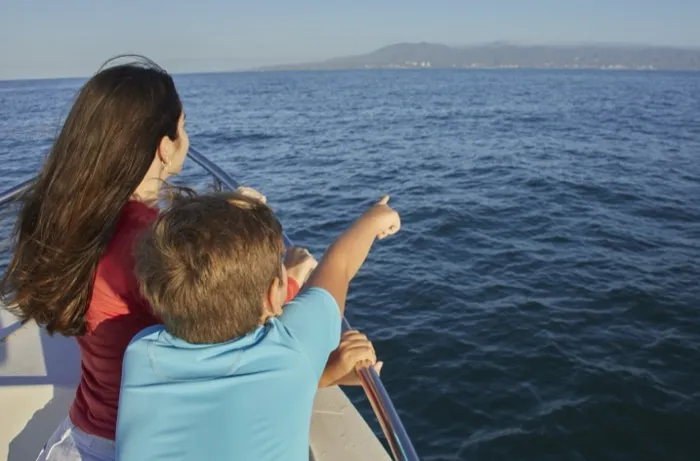 Mother and son pointing out to sea from the bow of a tour boat